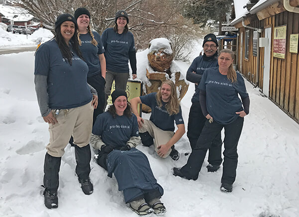 Seven staff modeling Academy T-shirts in the snow.